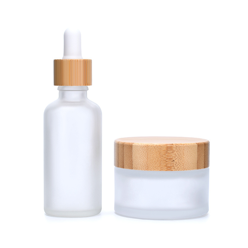 A set of frosted clear amber black personal skin care glass dropper bottles and glass jar with bamboo lid