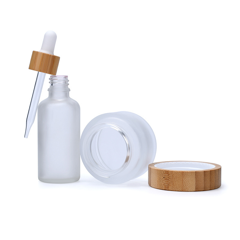 A set of frosted clear amber black personal skin care glass dropper bottles and glass jar with bamboo lid