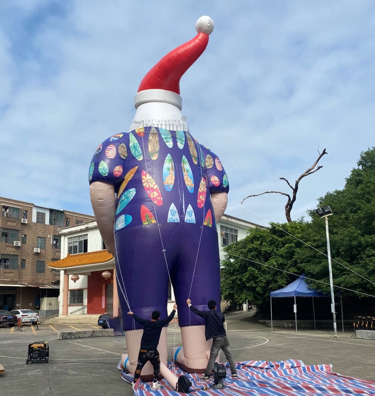 Giant inflatable Santa Claus surfing on the beach outdoors with a skateboard, beach themed Xmas inflatable decoration